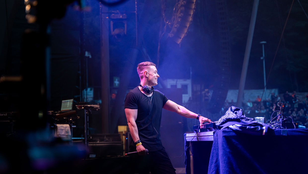 Tiscore DJing live on stage, focused at the decks during a packed club night.
