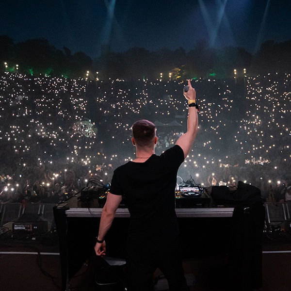 Tiscore raising his hand behind the DJ booth as thousands of fans light up the night.